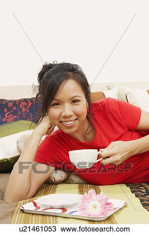 Portrait of a young woman lying on the bed and holding a cup of tea View Large Photo Image Stock Image - Portrait of a young woman lying on the bed and holding a cup of tea. Fotosearch