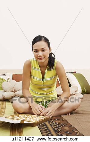 Stock Photo - Portrait of a young woman sitting on the bed and smiling. Fotosearch