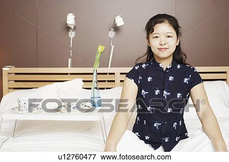 Stock Photo - Portrait of a young woman sitting cross-legged on the bed smiling. Fotosearch