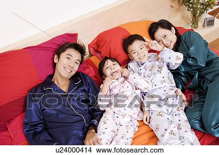Portrait of two parents lying on the bed with their two children View Large Photo Image Picture - Portrait of two parents lying on the bed with their two children. Fotosearch