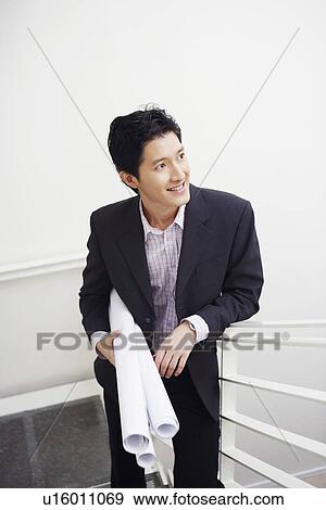 Stock Photo - Businessman walking up stairs and carrying blueprints. Fotosearch
