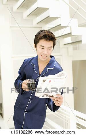Stock Photograph - Close-up of a mid adult man holding a cup of coffee and reading newspaper. Fotosearch