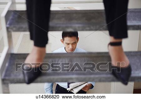 Low section view of a person standing on a staircase and a young man reading a newspaper in background View Large Photo Image Stock Image - Low section view of a person standing on a staircase and a young man reading a newspaper in background. Fotosearch