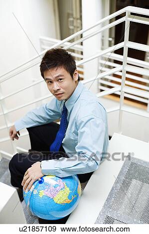 Stock Photo - Portrait of a businessman sitting on steps with a globe. Fotosearch