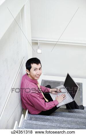 Stock Photo - Portrait of a businessman sitting on steps and using a laptop. Fotosearch