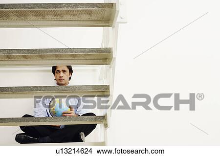 Portrait of a businessman sitting cross-legged on a step and holding a globe View Large Photo Image Picture - Portrait of a businessman sitting cross-legged on a step and holding a globe. Fotosearch