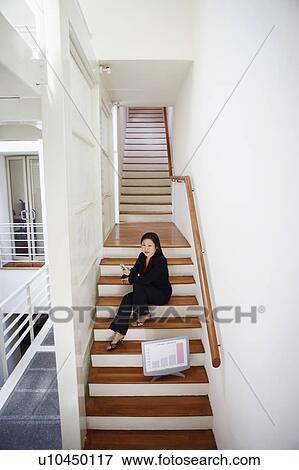 Stock Photo - Portrait of a businesswoman sitting on a staircase and holding a mobile phone. Fotosearch