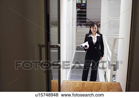 Stock Photo - Portrait of a female architect holding rolled up blueprints and smiling. Fotosearch