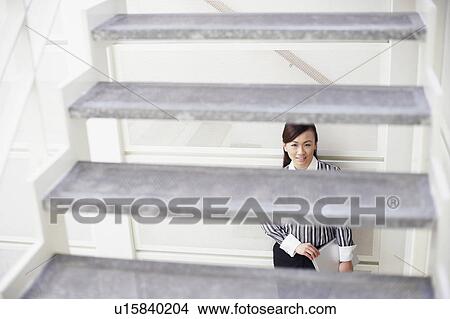 Portrait of a young woman leaning against a wall and holding a laptop View Large Photo Image Picture - Portrait of a young woman leaning against a wall and holding a laptop. Fotosearch
