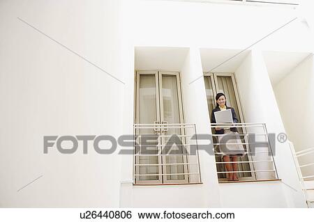 Stock Photograph - Portrait of a young woman standing at the doorway of an office and using a laptop. Fotosearch