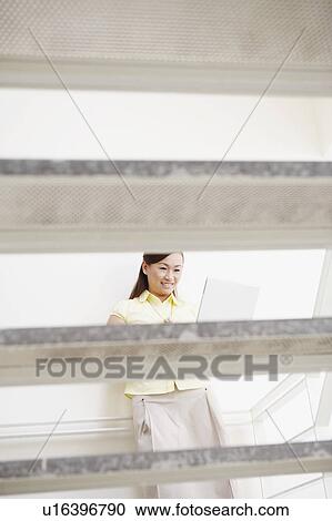 Young woman leaning against a wall and using a laptop View Large Photo Image Stock Image - Young woman leaning against a wall and using a laptop. Fotosearch