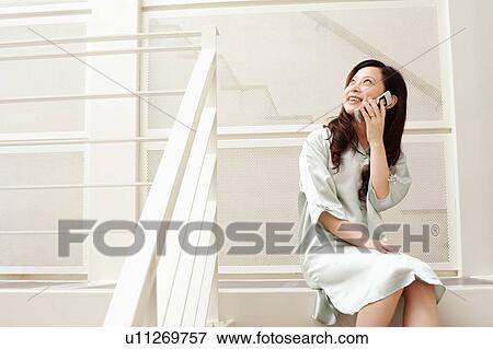 Stock Photo - Young woman sitting on a staircase and using a mobile phone. Fotosearch