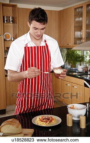 Stock Image - Man sprinkling cheese on spaghetti. Fotosearch