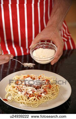 Stock Image - Man sprinkling cheese on spaghetti. Fotosearch
