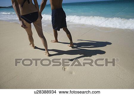 Low section of a couple walking on beach View Large Photo Image Picture - Low section of a couple walking on beach. Fotosearch