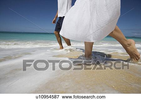 Stock Photo - Low section of a couple walking on beach. Fotosearch