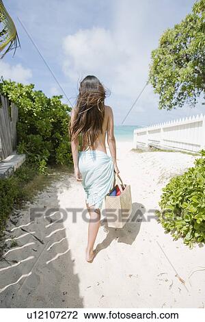 Stock Image - Rear view of a woman walking at beach. Fotosearch