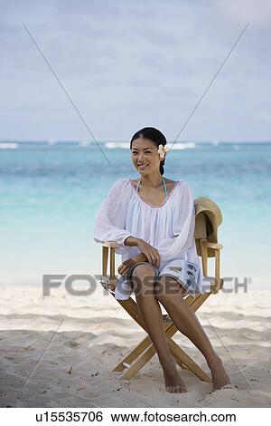Stock Photograph - A young woman sitting and smiling on chair at beach. Fotosearch