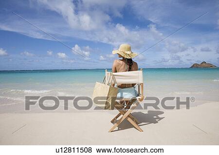 Rear view of a woman sitting on chair at beach View Large Photo Image Stock Photo - Rear view of a woman sitting on chair at beach. Fotosearch