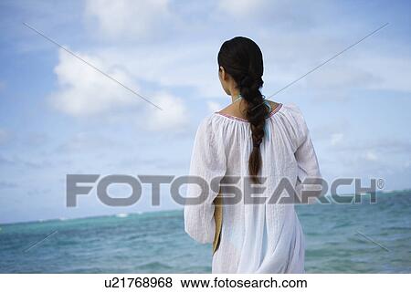 Rear view of a woman standing at beach View Large Photo Image Stock Photo - Rear view of a woman standing at beach. Fotosearch