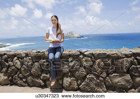 View of a young woman sitting on rock with book View Large Photo Image Stock Image - View of a young woman sitting on rock with book. Fotosearch