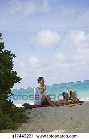 Stock Image - A woman holding wineglass and sitting at beach. Fotosearch