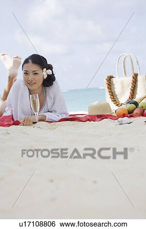 Stock Photograph - A young woman lying on sand at beach. Fotosearch
