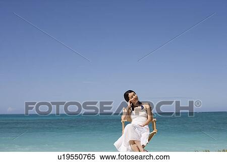 Stock Photography - A young woman sitting on chair at beach. Fotosearch