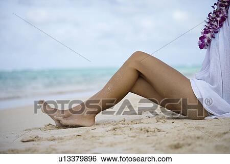 Stock Photograph - Low section of a woman sitting on sand at beach. Fotosearch