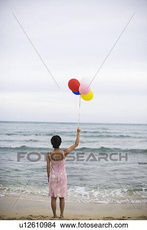 Rear view of a woman holding balloons at beach View Large Photo Image Picture - Rear view of a woman holding balloons at beach. Fotosearch