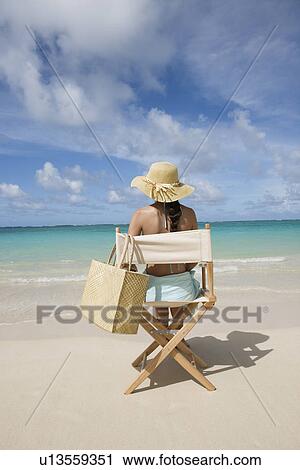 Rear view of a woman sitting on chair at beach View Large Photo Image Stock Image - Rear view of a woman sitting on chair at beach. Fotosearch