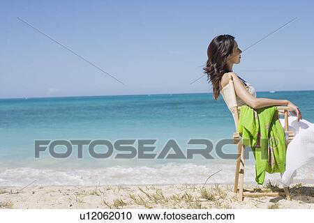 Side view of a young woman sitting on chair at beach View Large Photo Image Stock Image - Side view of a young woman sitting on chair at beach. Fotosearch