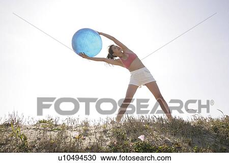 A young woman holds a huge ball as she bends from her abs while exercising View Large Photo Image Stock Image - A young woman holds a huge ball as she bends from her abs while exercising. Fotosearch