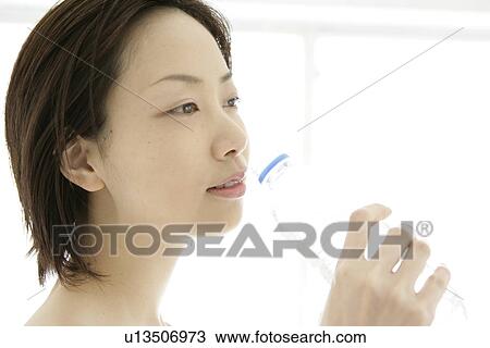 Stock Image - Side view of a young woman drinking water after her exercise. Fotosearch