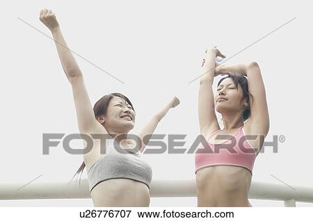 Two women wearing their workout suits stretch their arms in open air View Large Photo Image Stock Photo - Two women wearing their workout suits stretch their arms in open air. Fotosearch