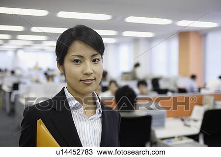 A professional woman holding a file smiles at the camera in the office View Large Photo Image Stock Image - A professional woman holding a file smiles at the camera in the office. Fotosearch