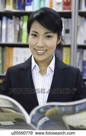 Stock Photo - A woman holding a book as she smiles at the camera. Fotosearch