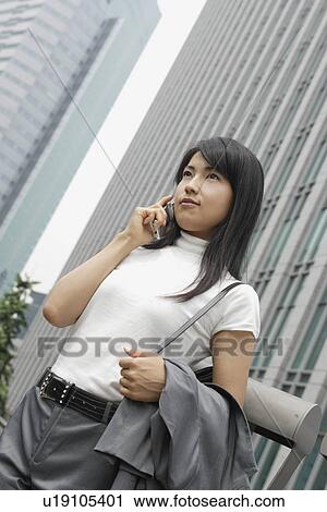 Stock Image - A woman seen conversing on the mobile phone amidst a commercial area. Fotosearch