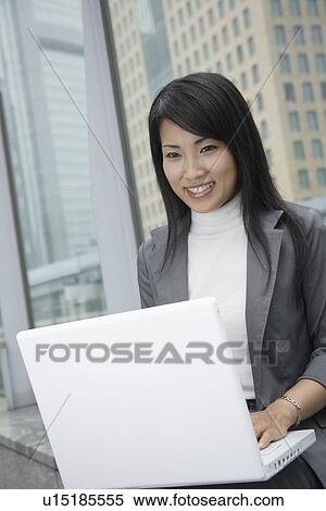 Stock Photography - A woman working over her laptop as she smiles at the camera. Fotosearch