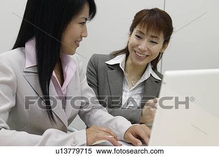 Two women enjoying themselves as they sit beside the laptop View Large Photo Image Stock Photography - Two women enjoying themselves as they sit beside the laptop. Fotosearch