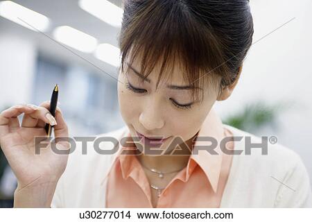Picture - Woman holds a pen as she reads something attentively. Fotosearch