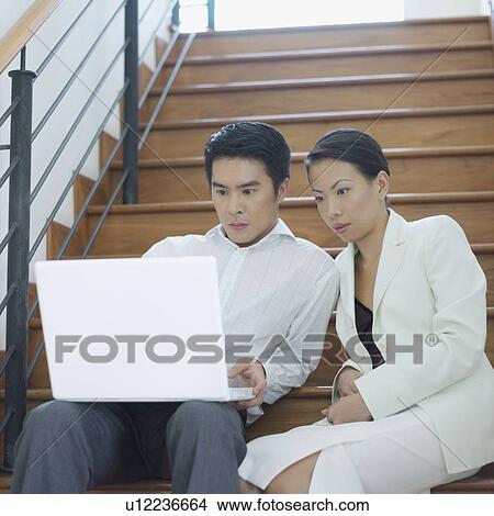 Businessman and businesswoman sitting on a staircase and looking at a laptop View Large Photo Image Picture - Businessman and businesswoman sitting on a staircase and looking at a laptop. Fotosearch
