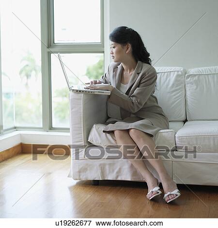 Businesswoman sitting on a couch using a laptop View Large Photo Image Stock Photo - Businesswoman sitting on a couch using a laptop. Fotosearch