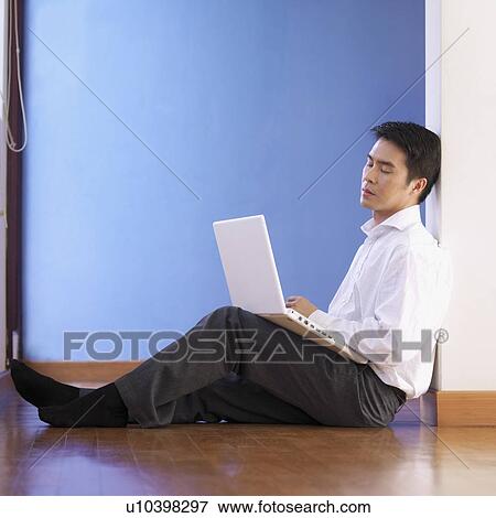 Side profile of a businessman sitting on the floor holding a laptop View Large Photo Image Stock Photo - Side profile of a businessman sitting on the floor holding a laptop. Fotosearch