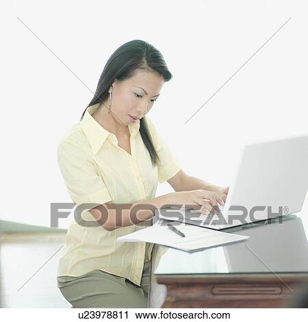 Stock Image - Side profile of a businesswoman working on a laptop. Fotosearch
