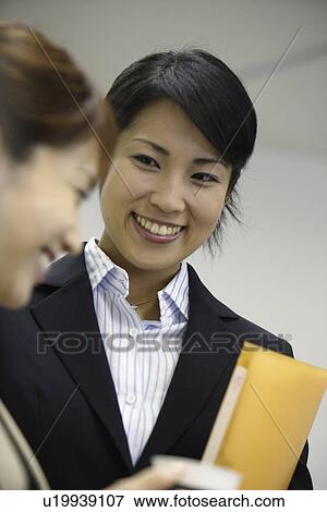 A woman holding a file shares a happy moment with her colleague View Large Photo Image Stock Photo - A woman holding a file shares a happy moment with her colleague. Fotosearch