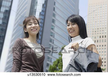 Two women smiling by looking at something in a commercial area View Large Photo Image Stock Image - Two women smiling by looking at something in a commercial area. Fotosearch