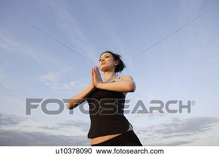 Stock Image - Low angle view of young woman performing yoga. Fotosearch