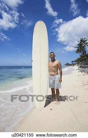 Man standing with surfboard on beach View Large Photo Image Stock Photography - Man standing with surfboard on beach. Fotosearch