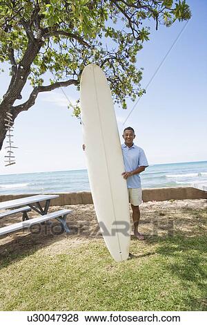 Stock Photo - Mature man standing with surfboard. Fotosearch